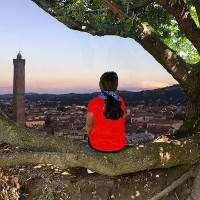 Una giovane donna guarda Bologna dall'alto seduta su un tronco d'albero