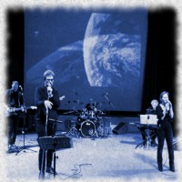 il gruppo dei musicisti durante lo spettacolo con una immagine della luna proiettata sullo sfondo